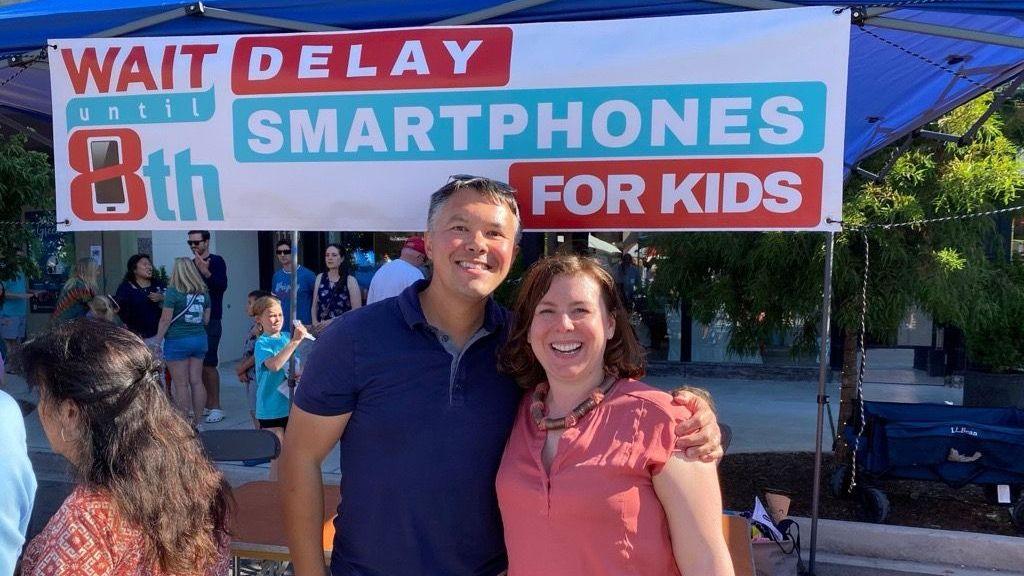 Mark SooHoo advocates for children to delay their use of smartphones. He stands with a woman in front of a banner that says Wait Until 8th