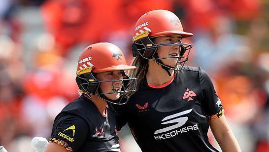 Alice Capsey (left) and Ellyse Perry, both wearing black tops and orange helmets