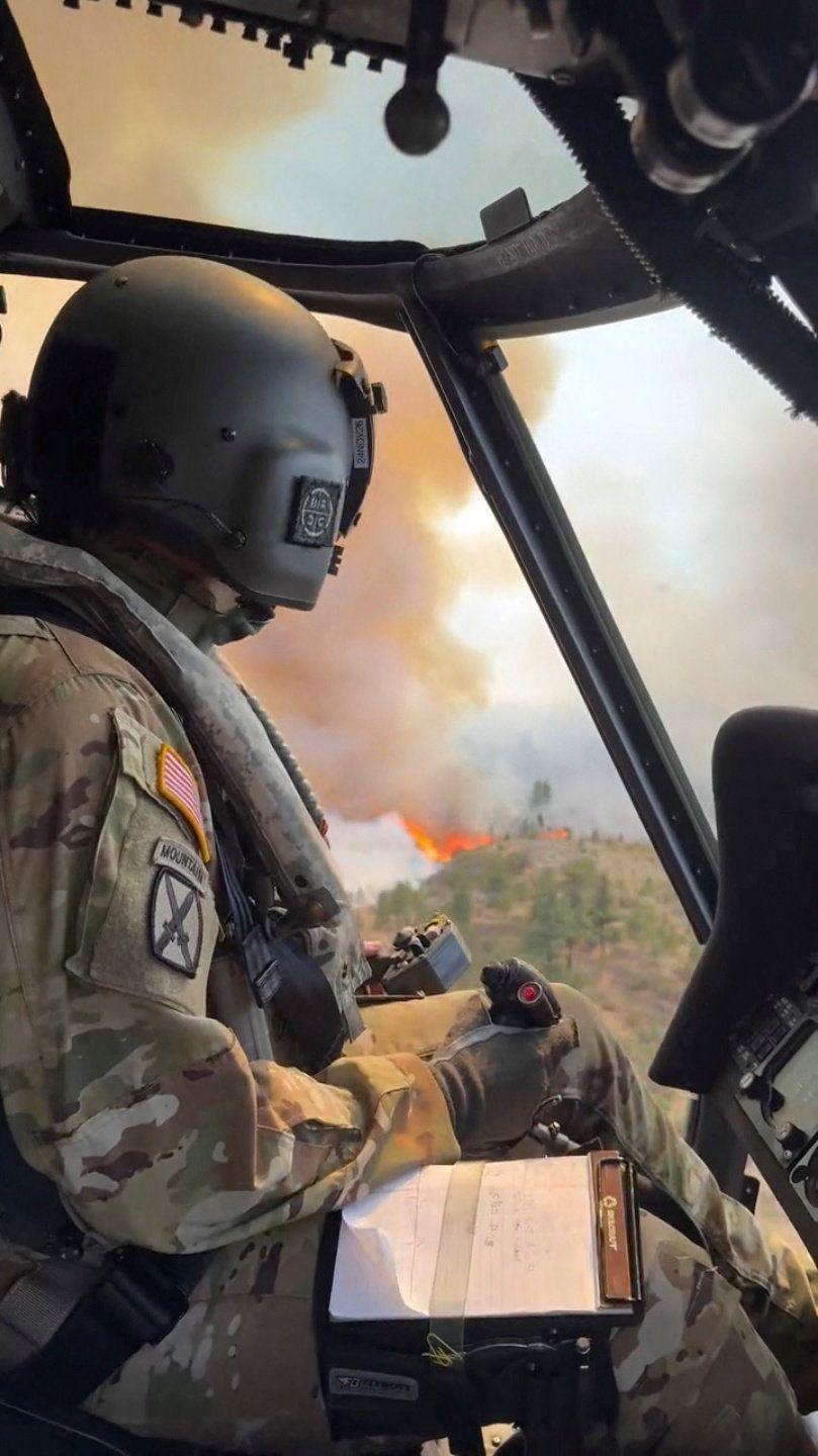An image taken from a video shows a National Guard member in a helicopter - in the background outside are flames and smoke billowing