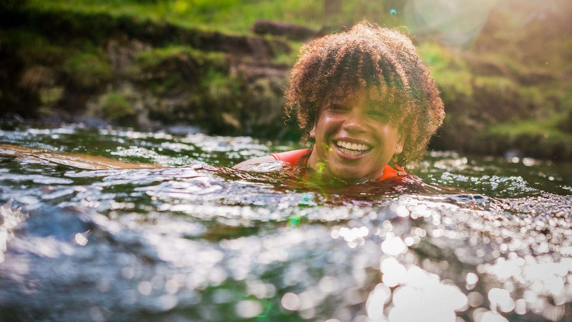 Cheerful young woman splashing water while enjoying swim with friends in sea on sunny day