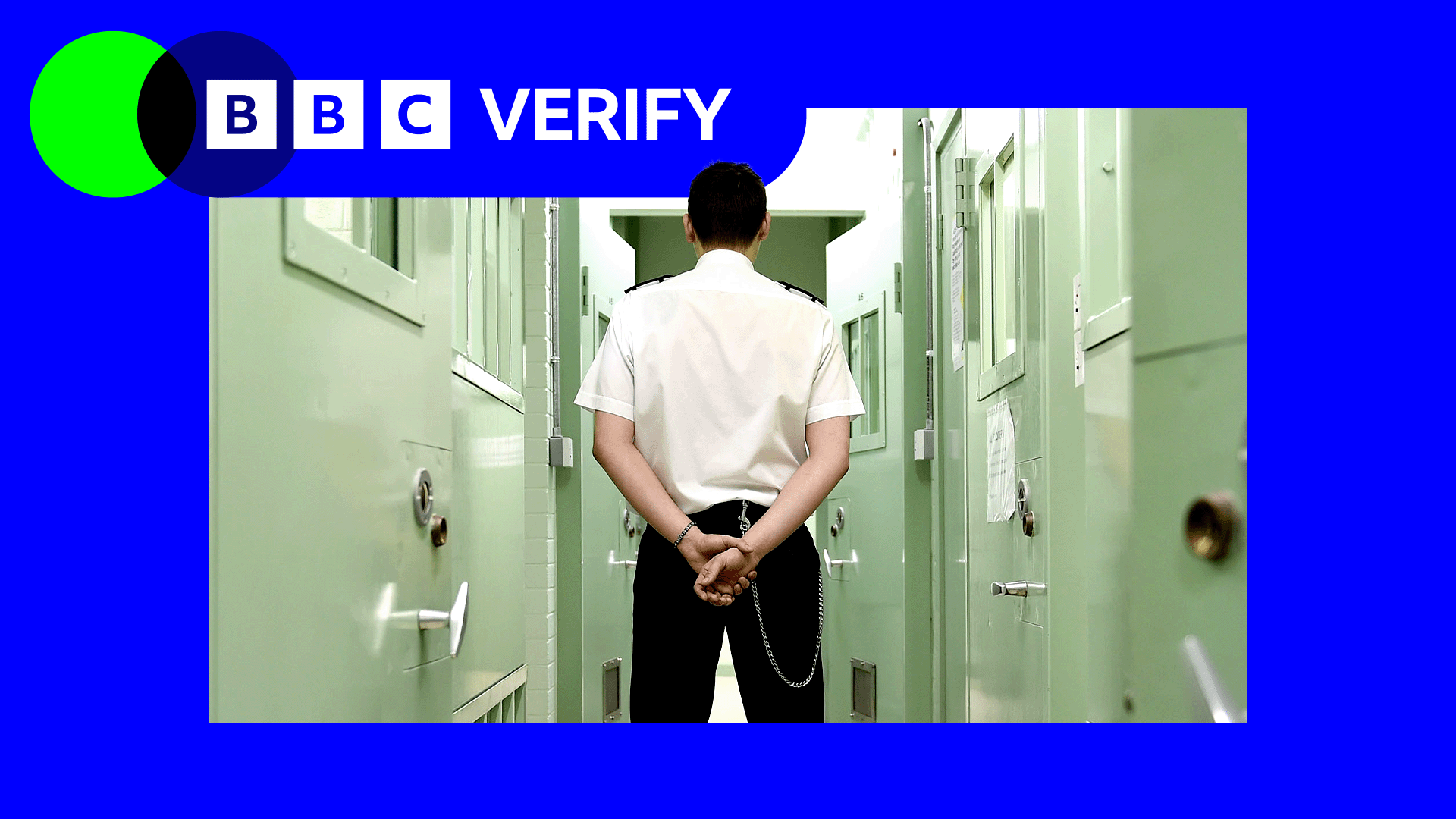 A prison officer wearing a white shirt and black trousers stands with his back to the camera. A row of green-painted cell doors are on either side
