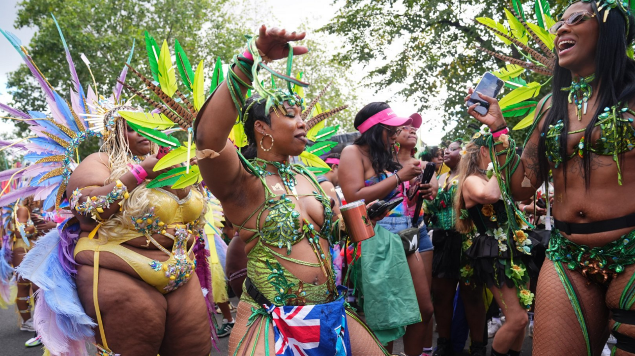 A group of women in feathered and beaded costumes dance in the street.