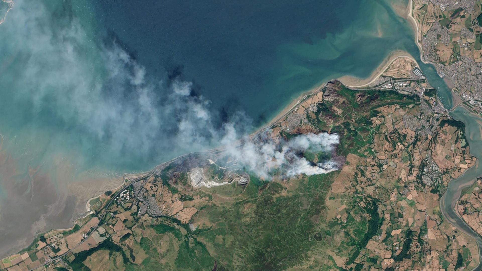 Aerial image of land with white smoke billowing from it.