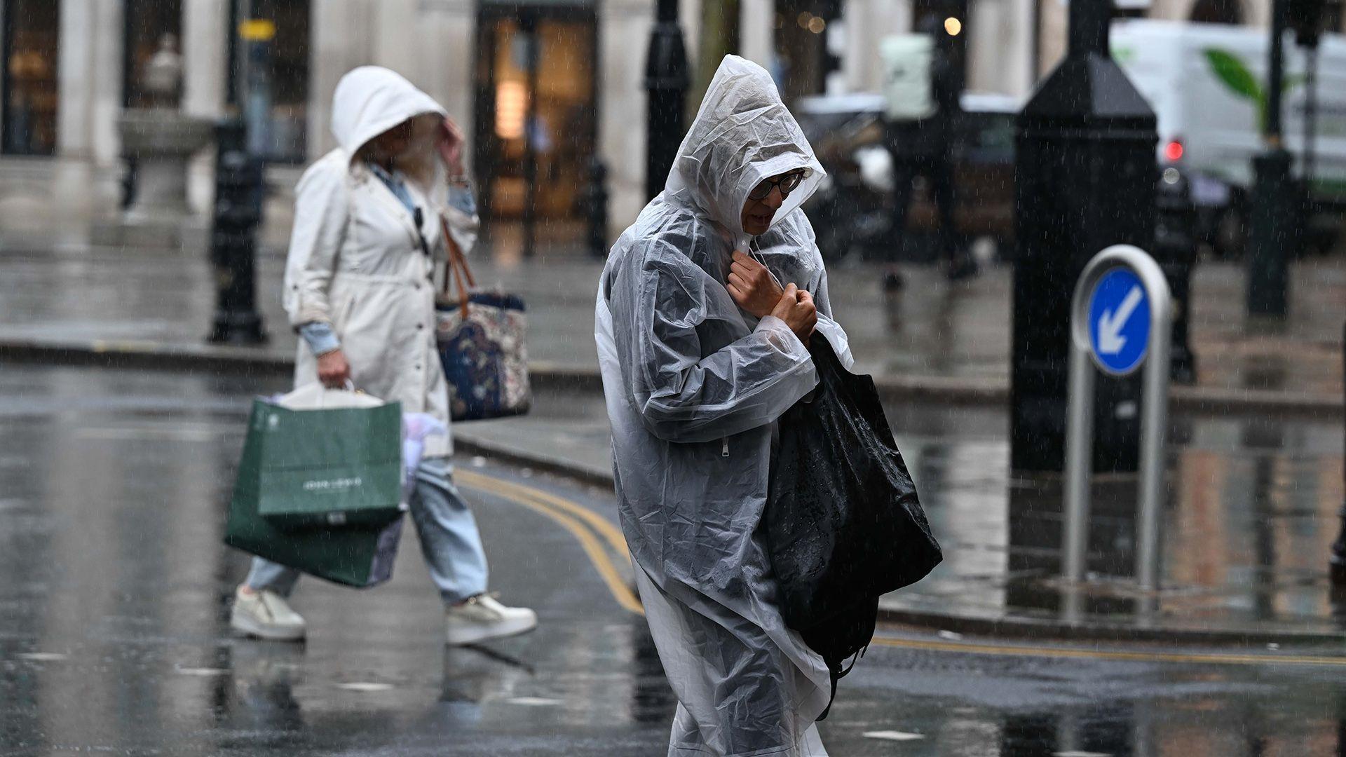 People wrapped in rain macs walk down a street in London carrying bags earlier in the summer.