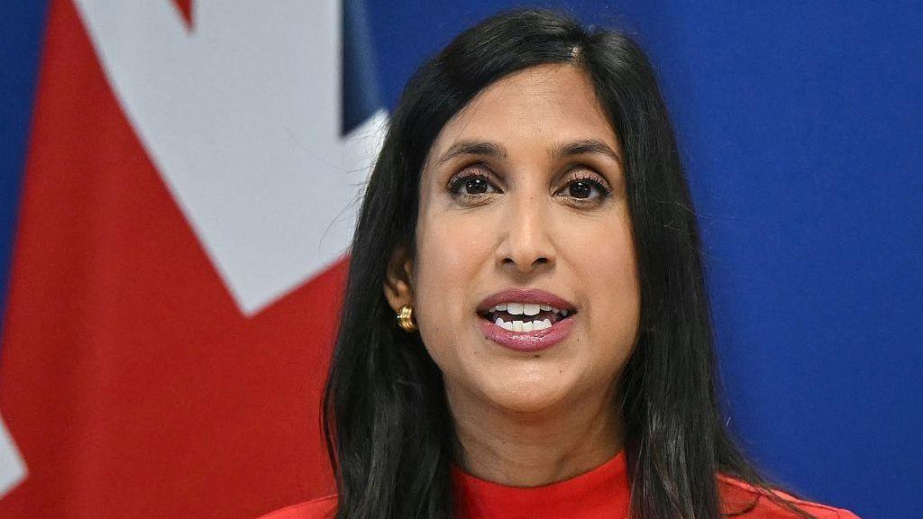 Claire Coutinho speaks during a party press conference in central London. In the background is a UK flag
