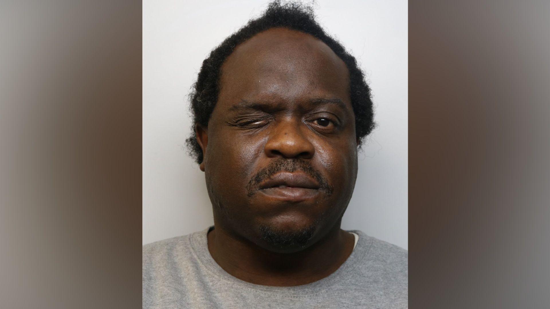 Close-up custody photograph of Levy wearing a light grey sweatshirt against a plain light-coloured background. The image is tightly cropped around the head and shoulders. One eye is partially closed, and Levy is facing the camera.
