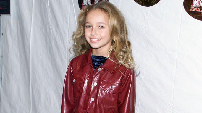 Panettiere pictured smiling at 11-years-old at a film premiere. She has curly dark blonde hair and wears a vinyl dark red jacket with a crused velvet blue top.