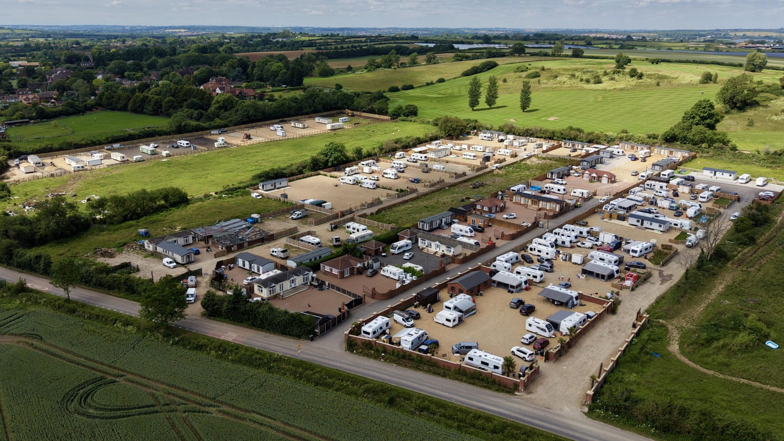 An aerial view of lots of caravans and static homes on brownfield land, surrounded by green fields.
