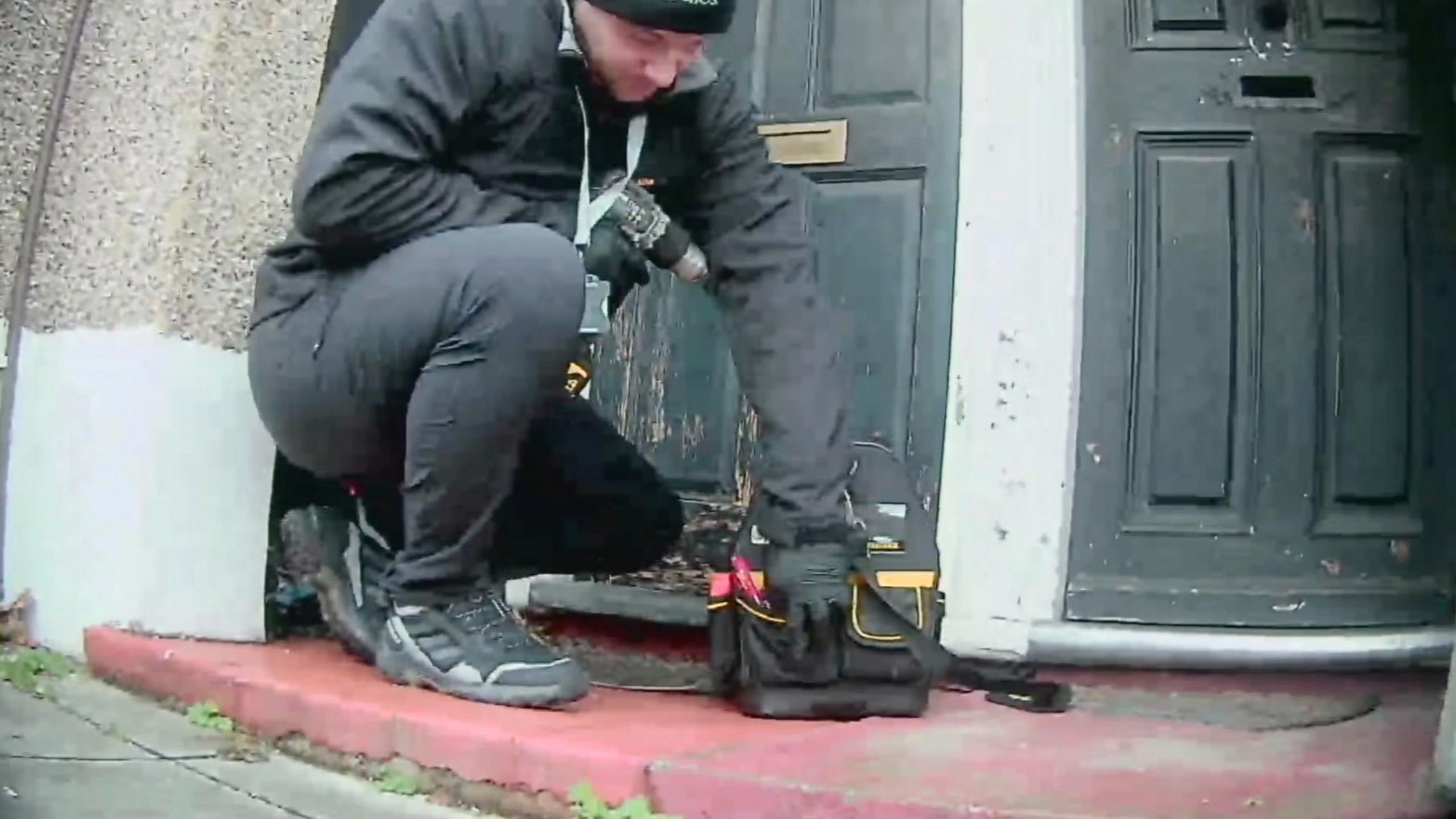 The man from 24/7 Locksmiths UK is holding his drill and is poised to drill the lock of a faded black painted door