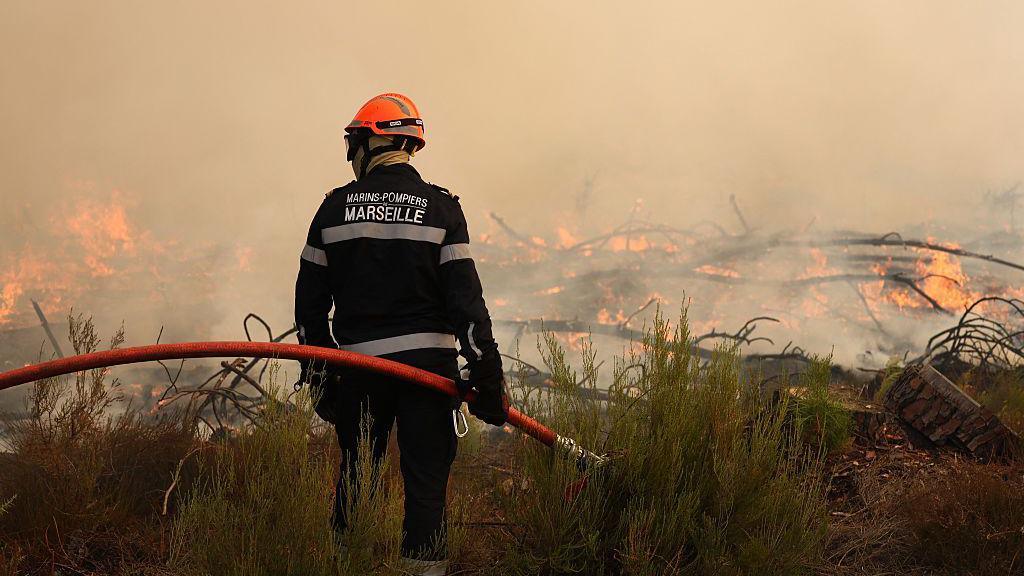 A firefighter holds a hose as he looks at burning vegetation
