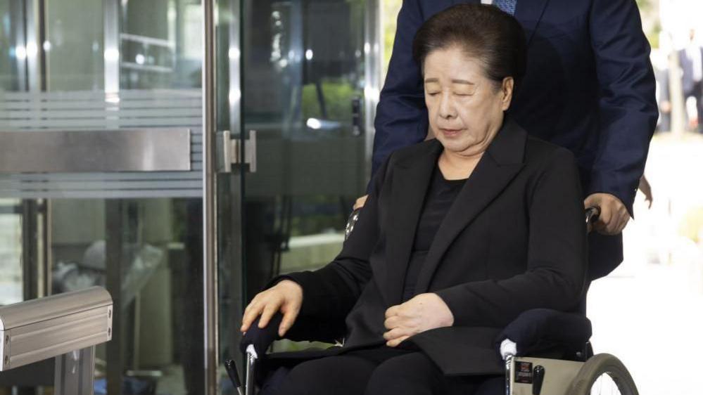 Unification Church leader Han Hak-ja, dressed in a black coat and seated on a wheelchair, arrives for an arrest warrant hearing on allegations of bribery and political funding, at the Seoul Central District Court in Seoul