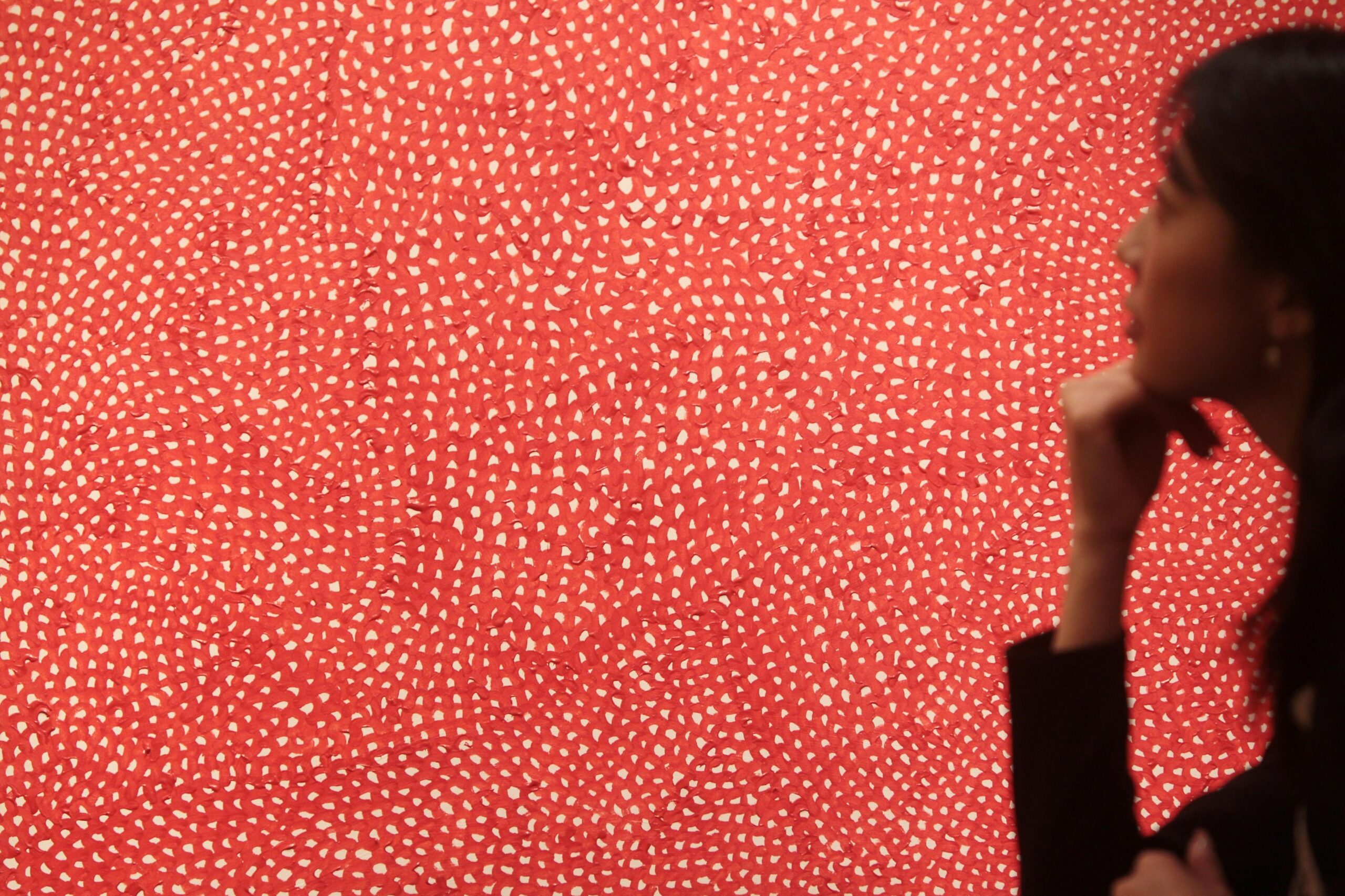 A red and white patterned artwork filling the photo with a woman looking at it at the edge