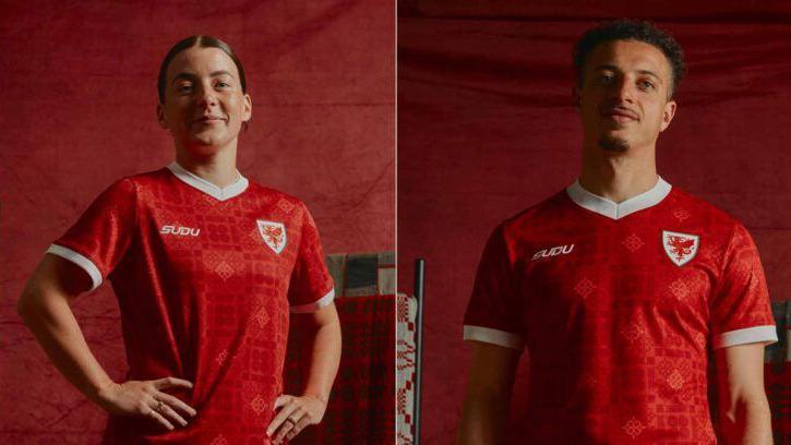 Angharad James-Turner and Ethan Ampadu stand side by side in a split portrait against a deep red backdrop, each wearing a bright red football shirt with white trim and a white crest featuring a red dragon on the chest. The shirt has a patterned design woven into the fabric. Angharad James-Turner on the left is shown from the waist up with one hand on her hip, while Ethan Ampadu faces the camera with their arms down. Studio lighting highlights the new team kit, with matching red tones throughout the image.