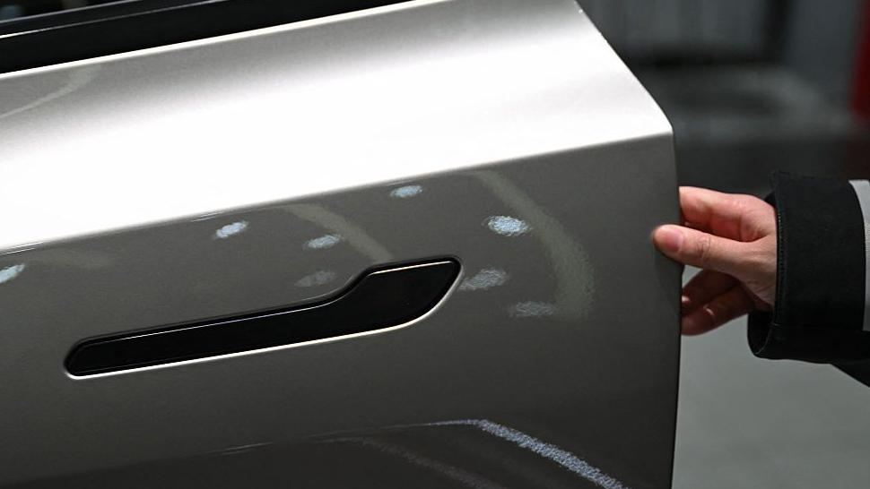 A customer inspects the minimalistic hidden door handles on an electric car in a showroom.