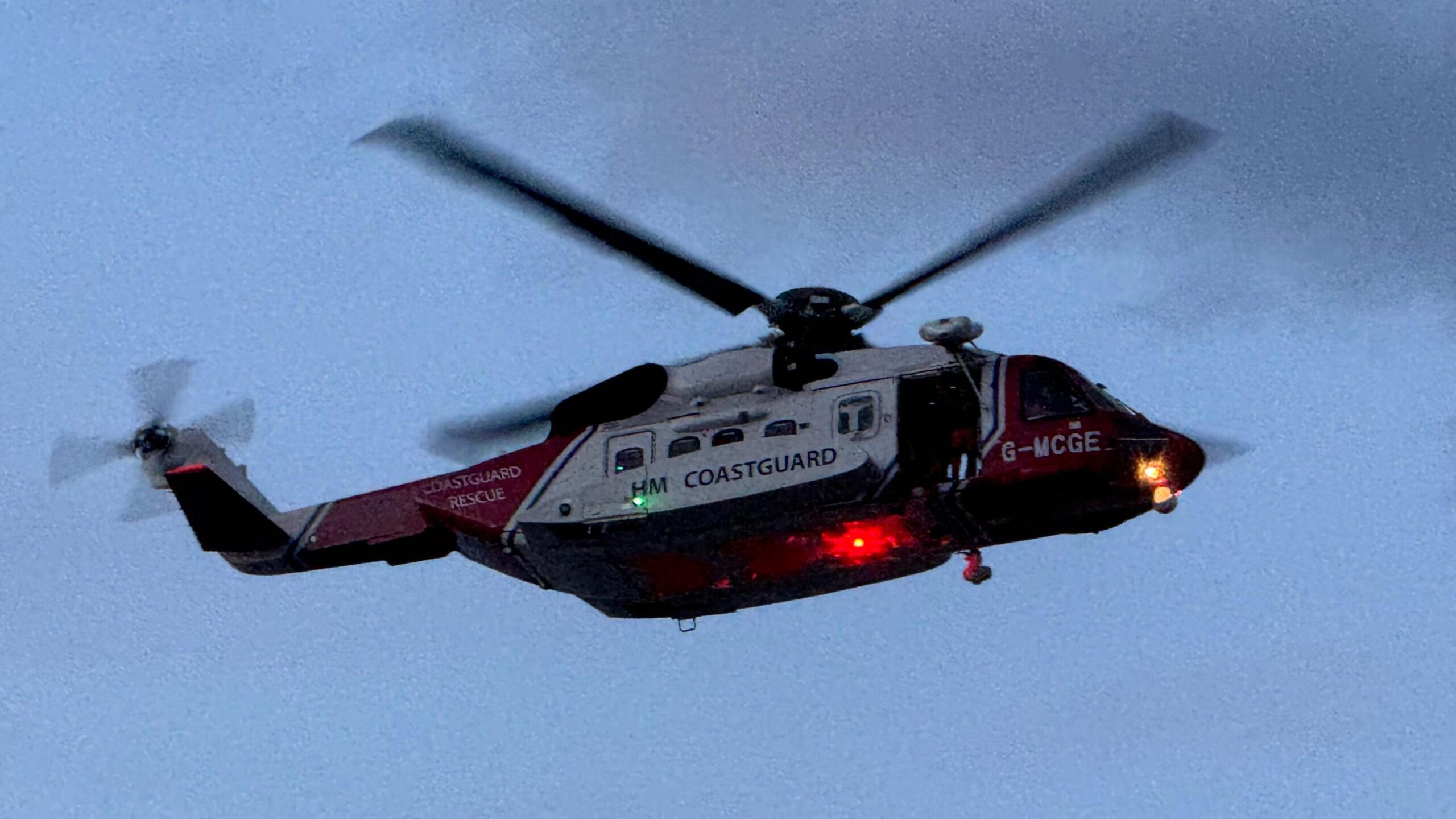 A HM Coastguard helicopter in the skies over Hornsea. It is red and white and has lights on its undercarriage.