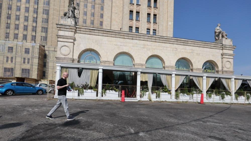 Man walking past the restaurant where the explosion happened, the glass windows are behind metal fencing.