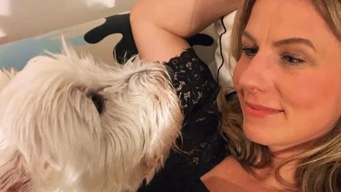 On the left, a white terrier sits on top of a woman with blonde hair lying on a sofa and looks up at her