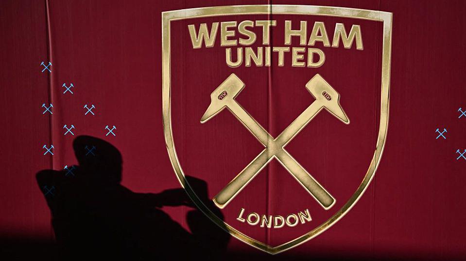 A silhouetted fan taking a picture of the West Ham badge
