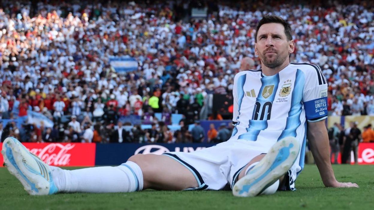 Lionel Messi sits on the pitch after the 2026 World Cup final, looking disappointed in Argentina kit