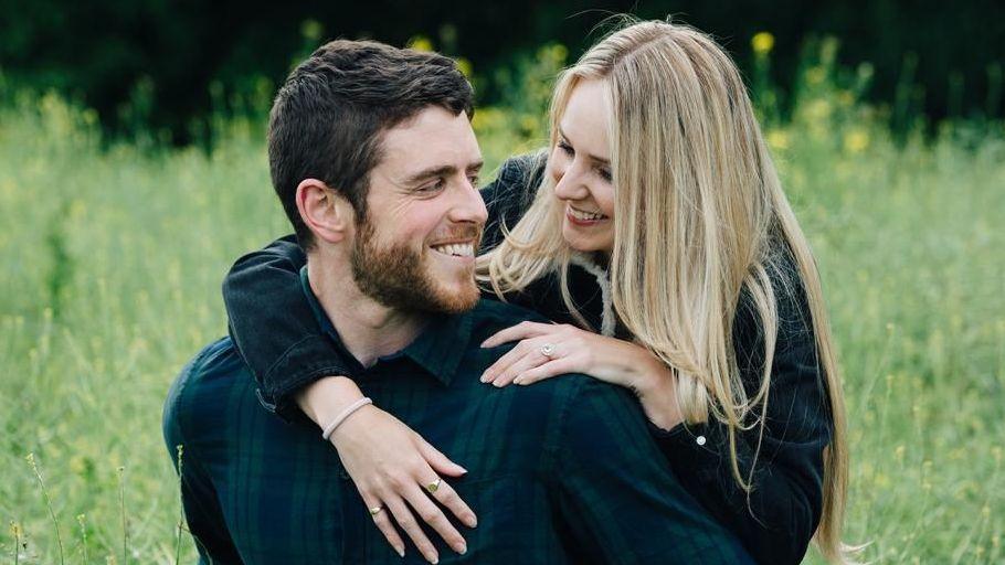 Andrew Harper and his fiance in a field, looking at each other and smiling