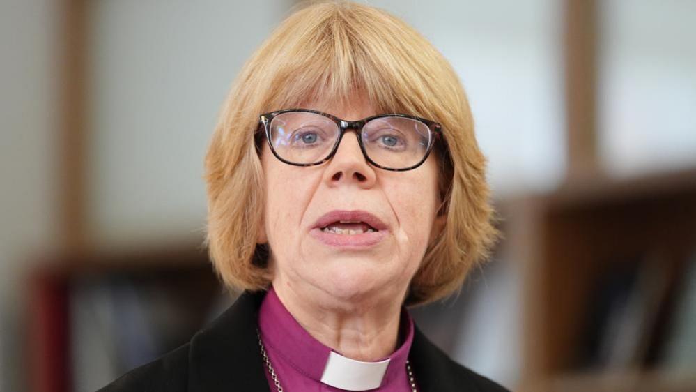 Dame Sarah Mullally, who has a blonde bob hairstyle with a fringe and wears glasses with a dark frame, is pictured speaking at a previous event at Chapter House in Canterbury Cathedral