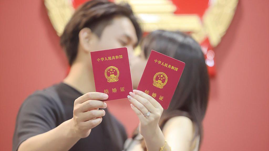 A newly-wed couple pose for a photo with their marriage certificates in Yangzhou, Jiangsu Province of China.
