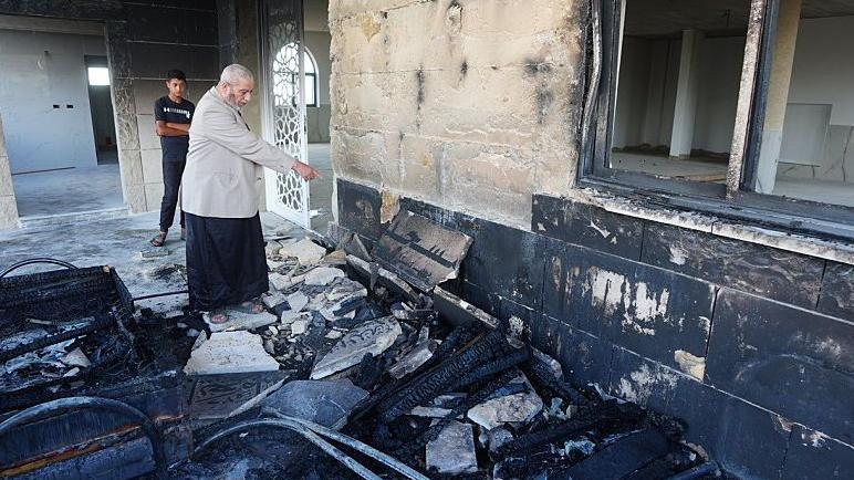 A view of the destruction on the exterior walls of Al-Rahmah Mosque as a Palestinian man points at damage