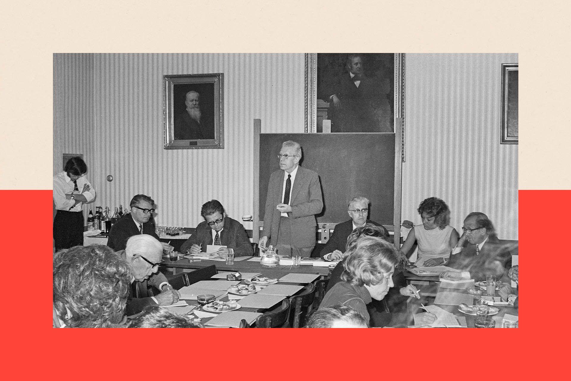 Hans Asperger standing up at a conference. He wears a light suit and is surrounded by other delegates. The photograph is black and white