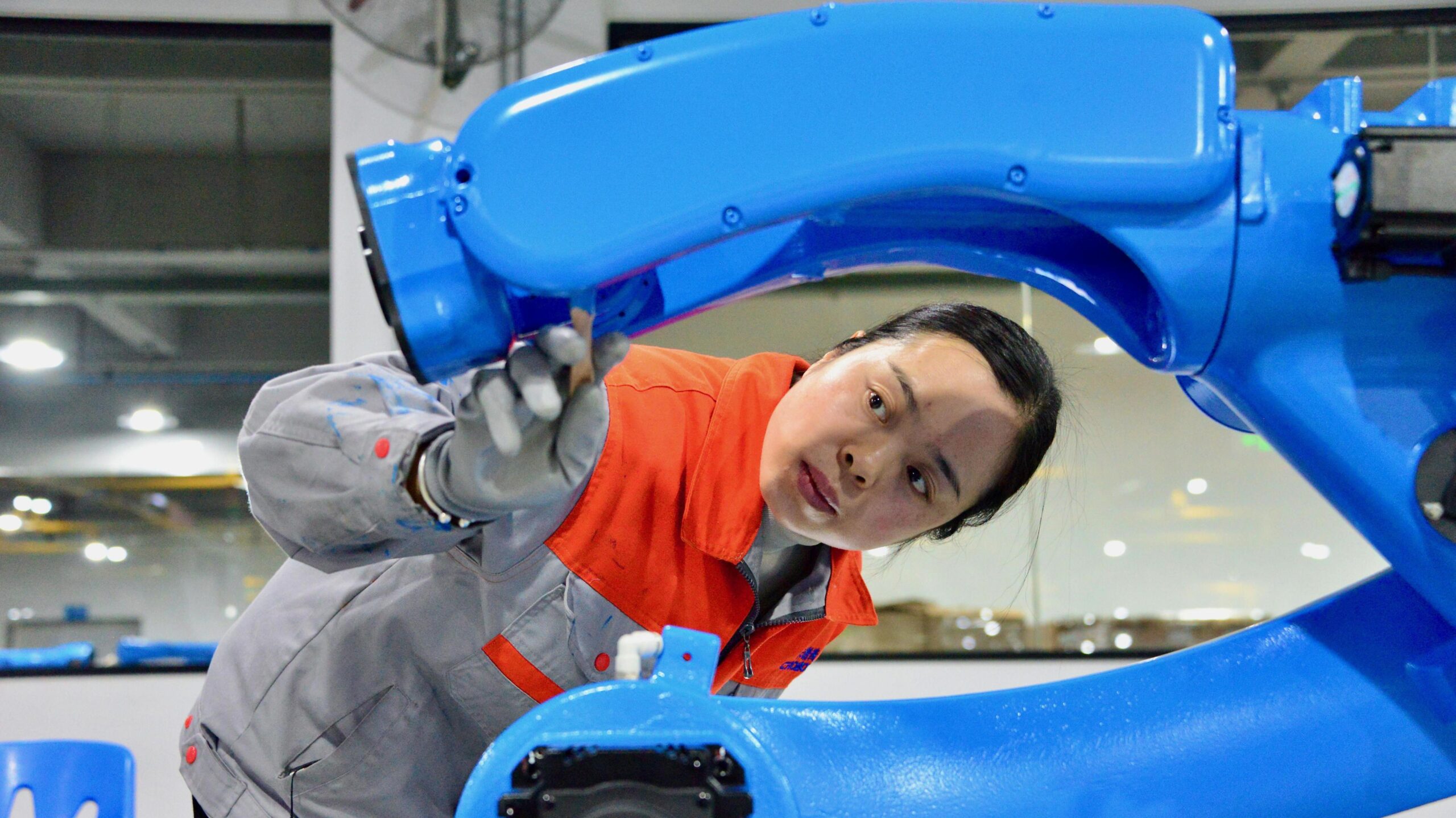 A young woman examining a blue robot arm