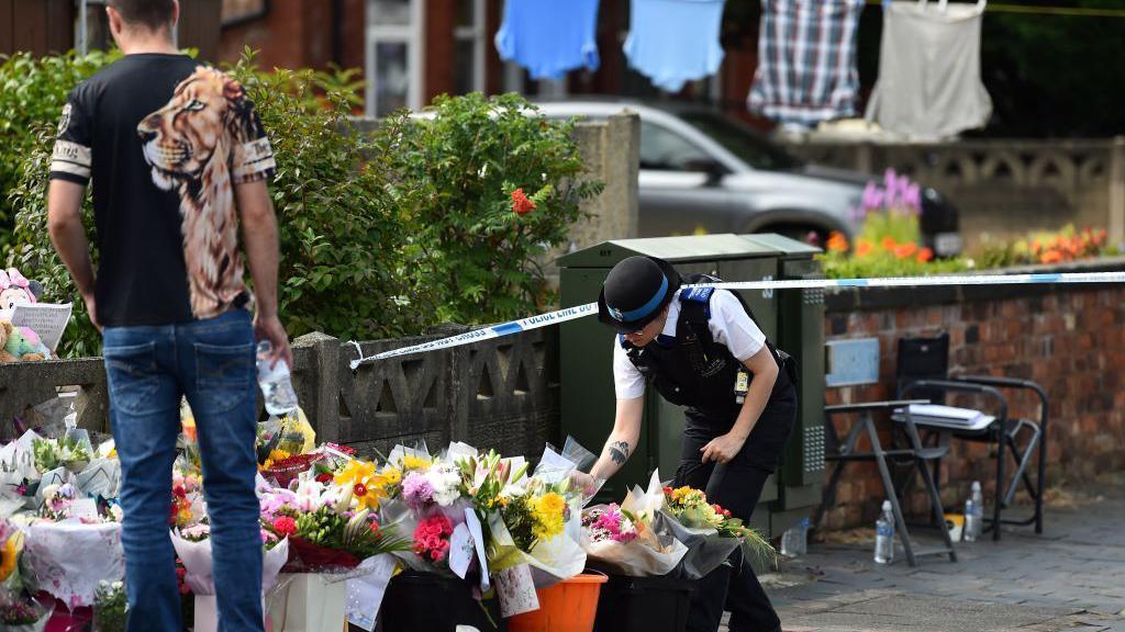 A police officer lays flowers as tributes are laid for the victims of a deadly knife attack in Southport, northwest England, on July 31, 2024.