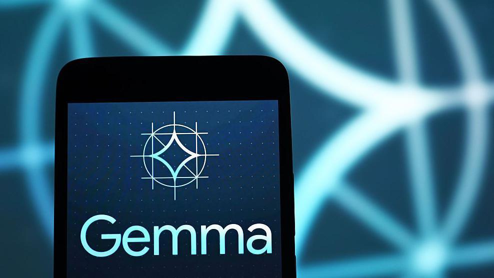 Google's Gemma logo displayed on a smartphone, against a backdrop of an enlarged, blurred version of the same logo.
