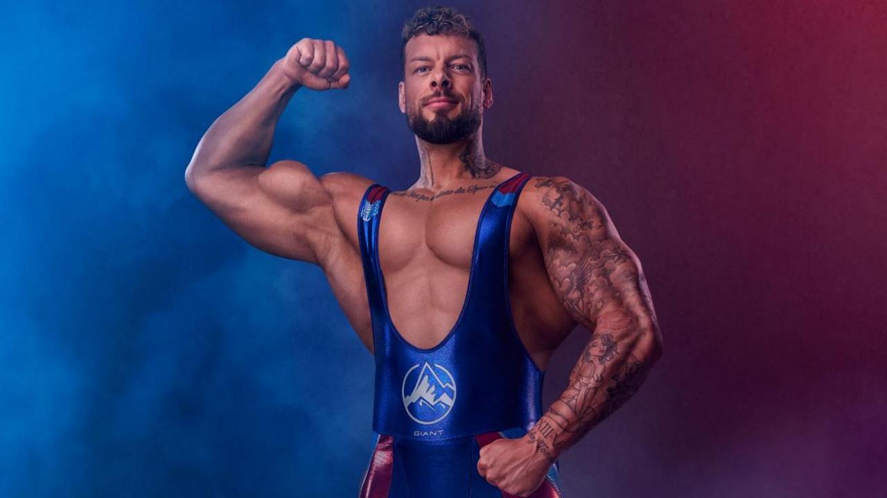 A man with extremely large biceps flexes his muscles in a blue and red leotard.
