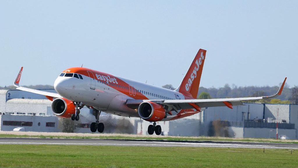 A white and orange easyJet plane landing on a runway.