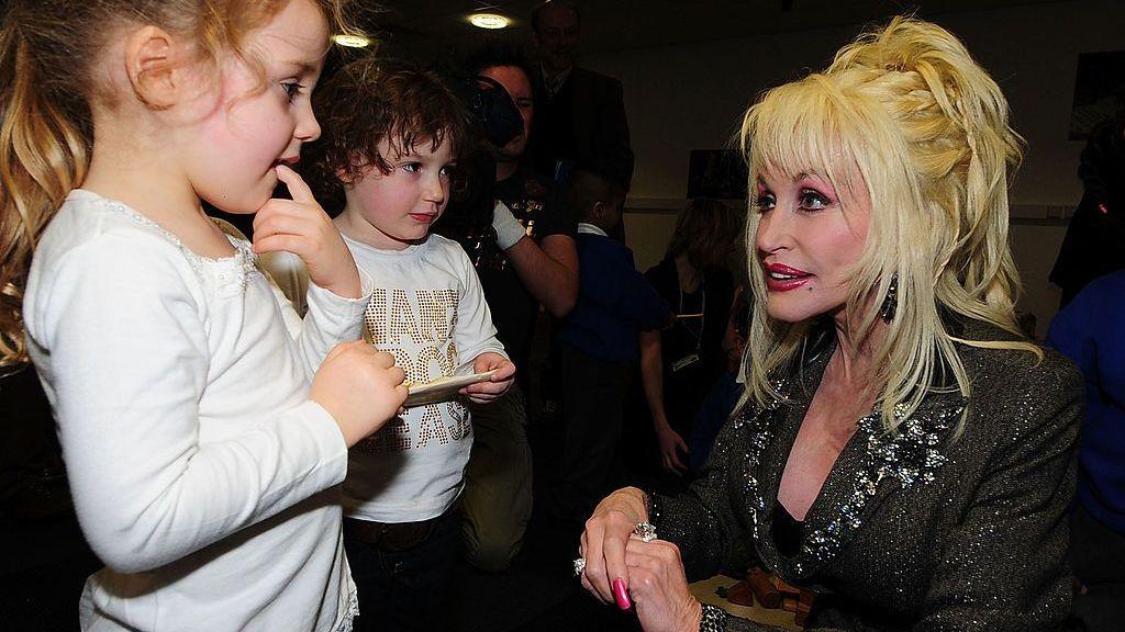 Dolly Parton crouches down to speak to two young children