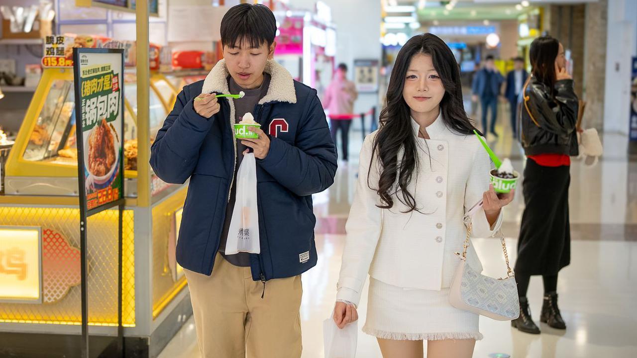 A young man and young woman in a food court. They are holding small green and white-coloured pots of dessert.