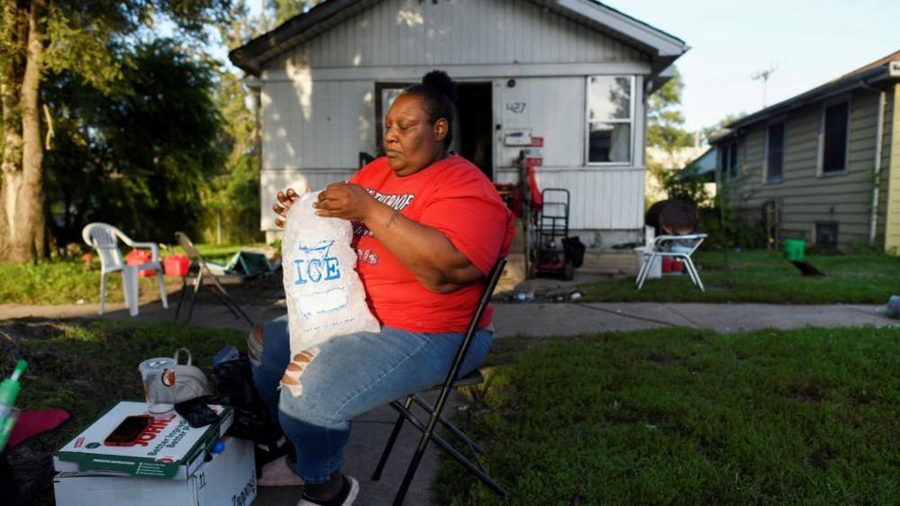 Dinky Austin gets ice to cool off with ice water, as thousands of residents remain without electricity more than a week after severe storms struck Gary, Indiana