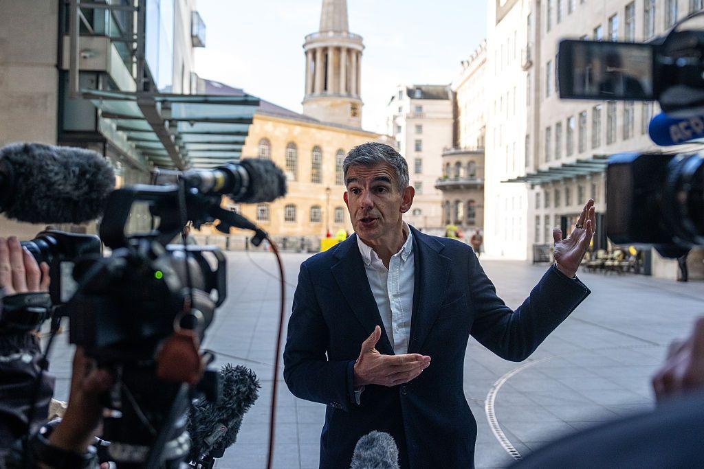 Picture of Matt Brittin stood outside the BBC, with cameras facing him. He wears a dark suit jacket with an open shirt and no tie.