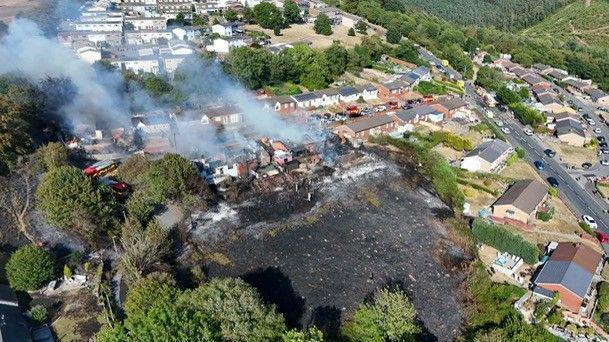 An aerial photo of the scene, showing the full extent of a blackened patch of land. The burned homes are on a resident street, with another row of housing behind.