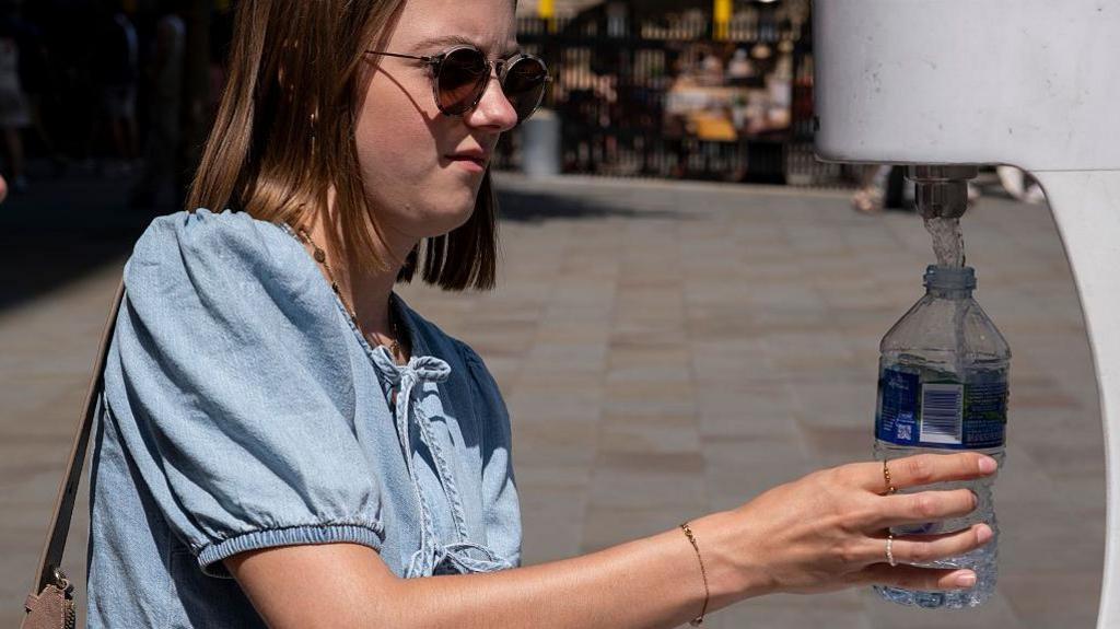 People using a water fountain to top up their water bottles in the Spring heat to keep cool and hydrated during the first heatwave of the year