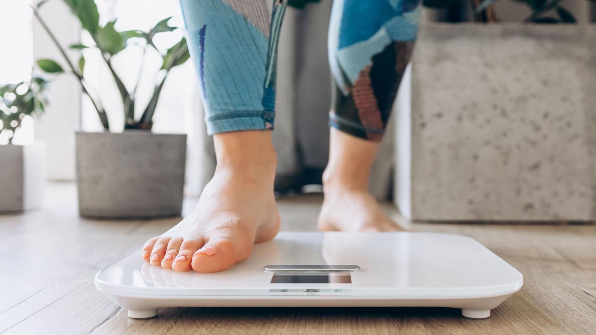 A woman in gym clothing steps on to electronic weighing scales at home