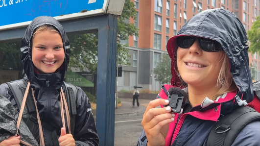 Tabby is wearing a waterproof coat and is wearing sunglasses. She is smiling. Evie is stood next to her and is also smiling. She is wearing a waterproof coat too.