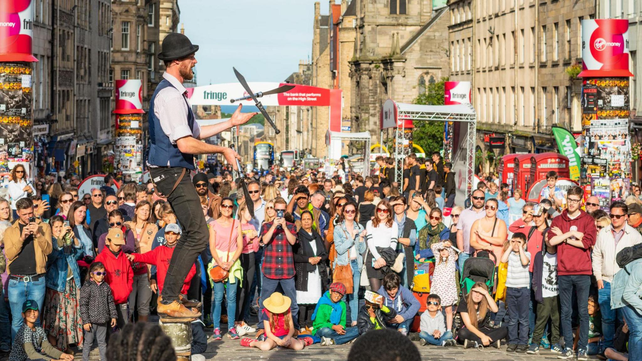 A man juggles knives on Edinburgh's Royal Mile, he is surrounded by hundreds of tourists and visitors