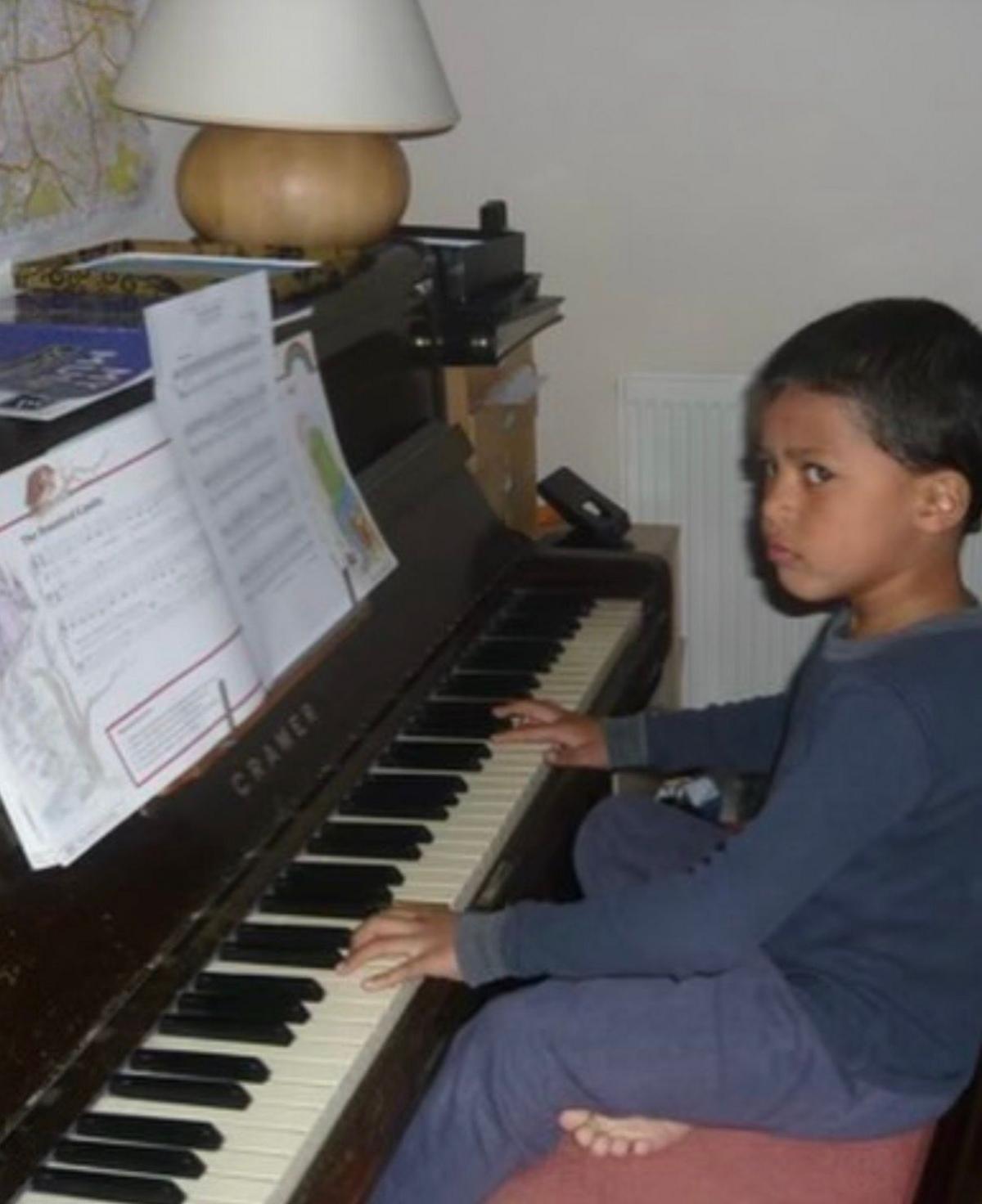 A young Kamal is playing the piano. He is wearing a navy tracksuit.