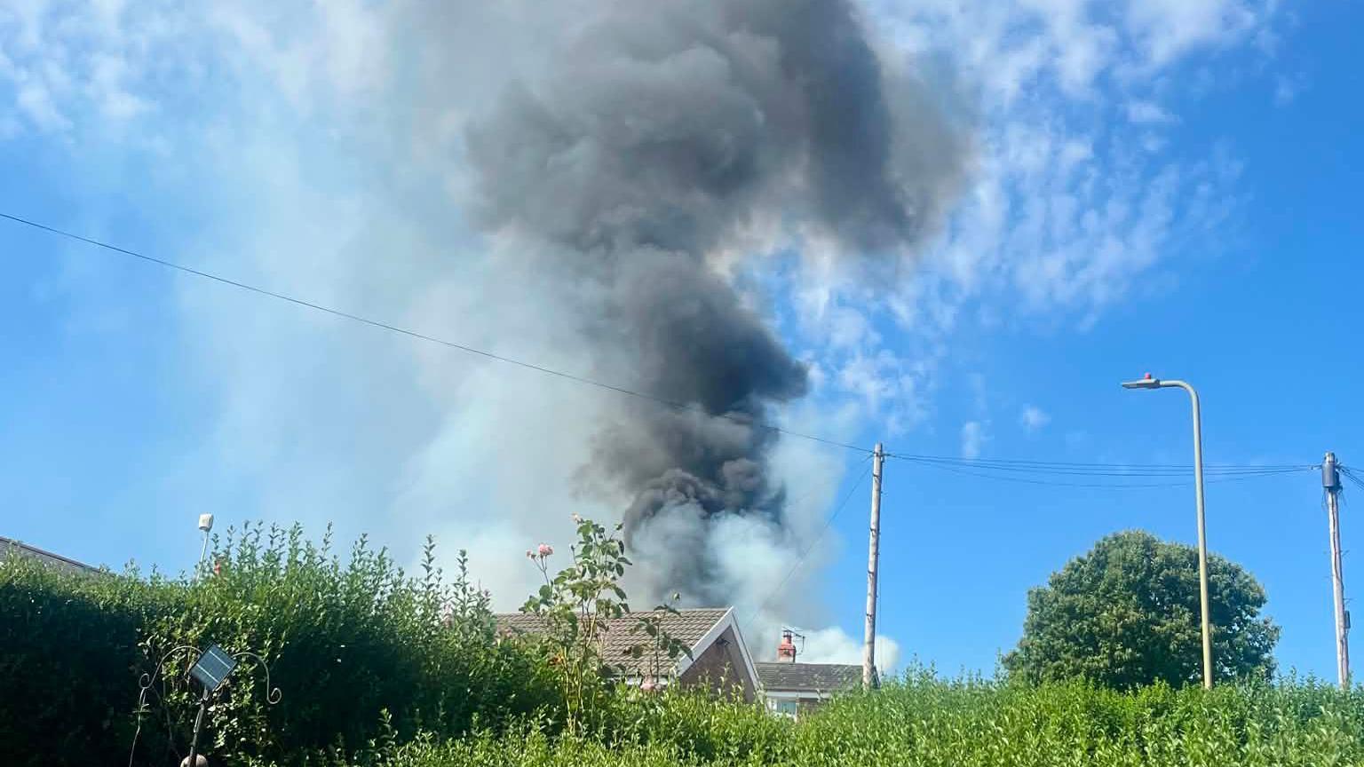 Black and grey smoke billows above the roofs of two houses.