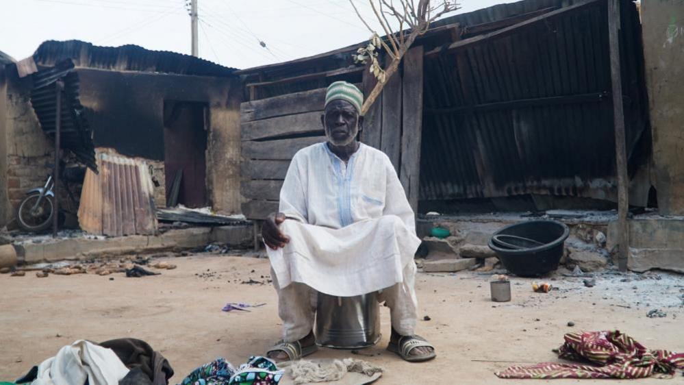 A man sits in front of burnt out remains in a Woro village in Nigeria