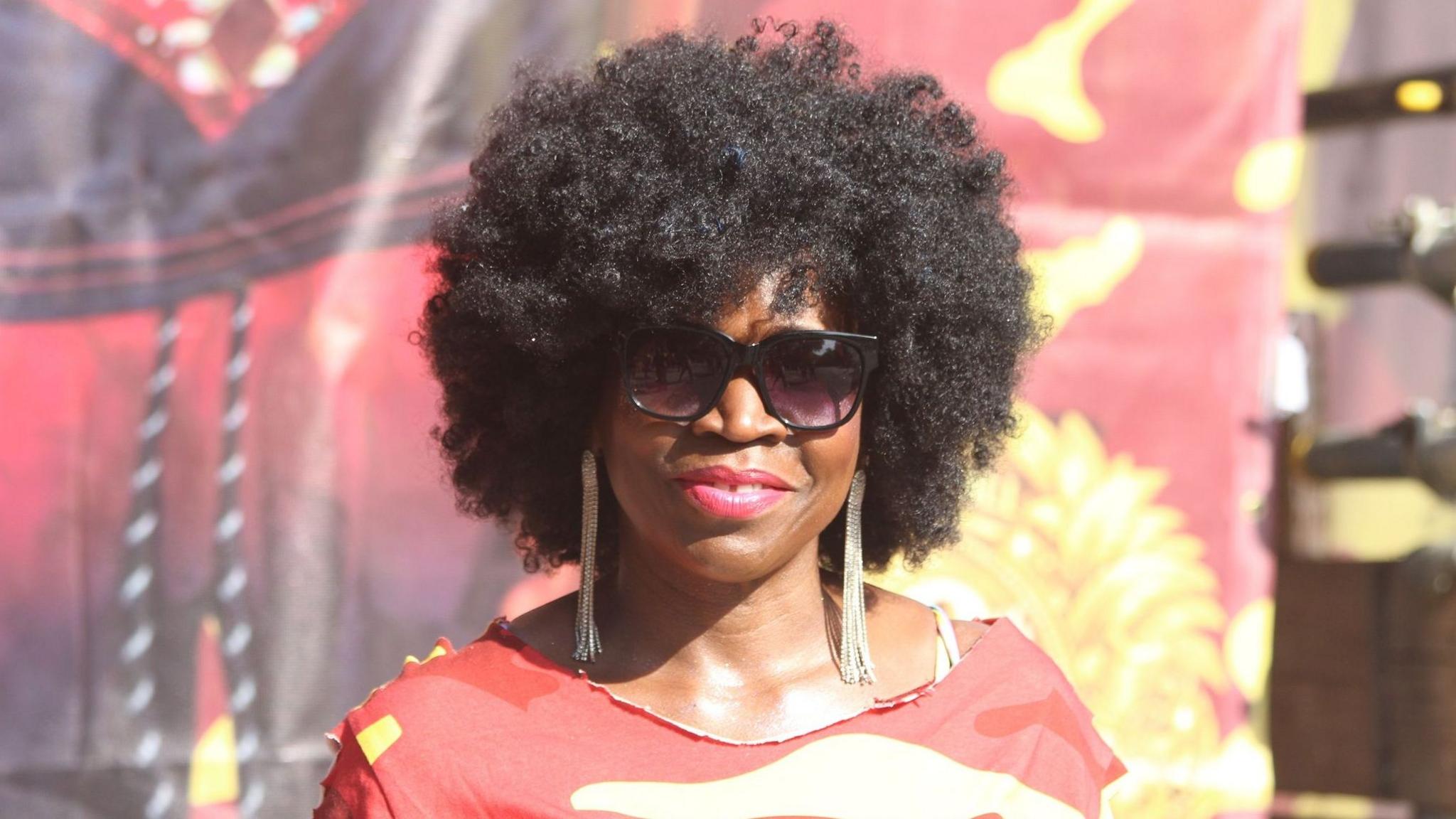 Heather, wearing a red top, smiles at the camera in the sunshine