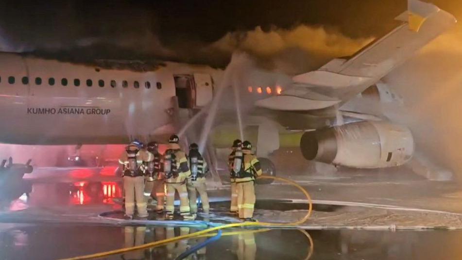 Six firefighters train hoses on the burning fuselage of a Air Busan plane at Gimhae Airport, South Korea.