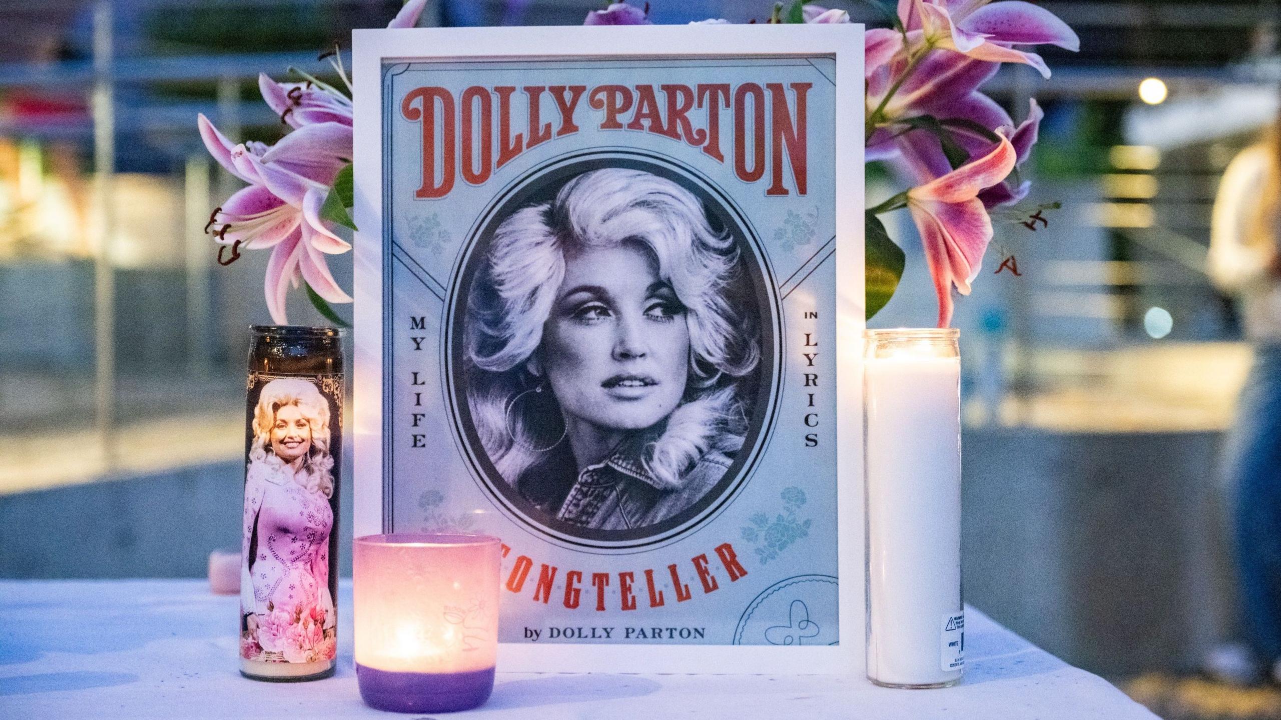 An illustration of Dolly Parton with her name stands on a table in front of a vase of pink lilies and behind three candles during the during a Seattle Community Vigil for Dolly Parton on Friday