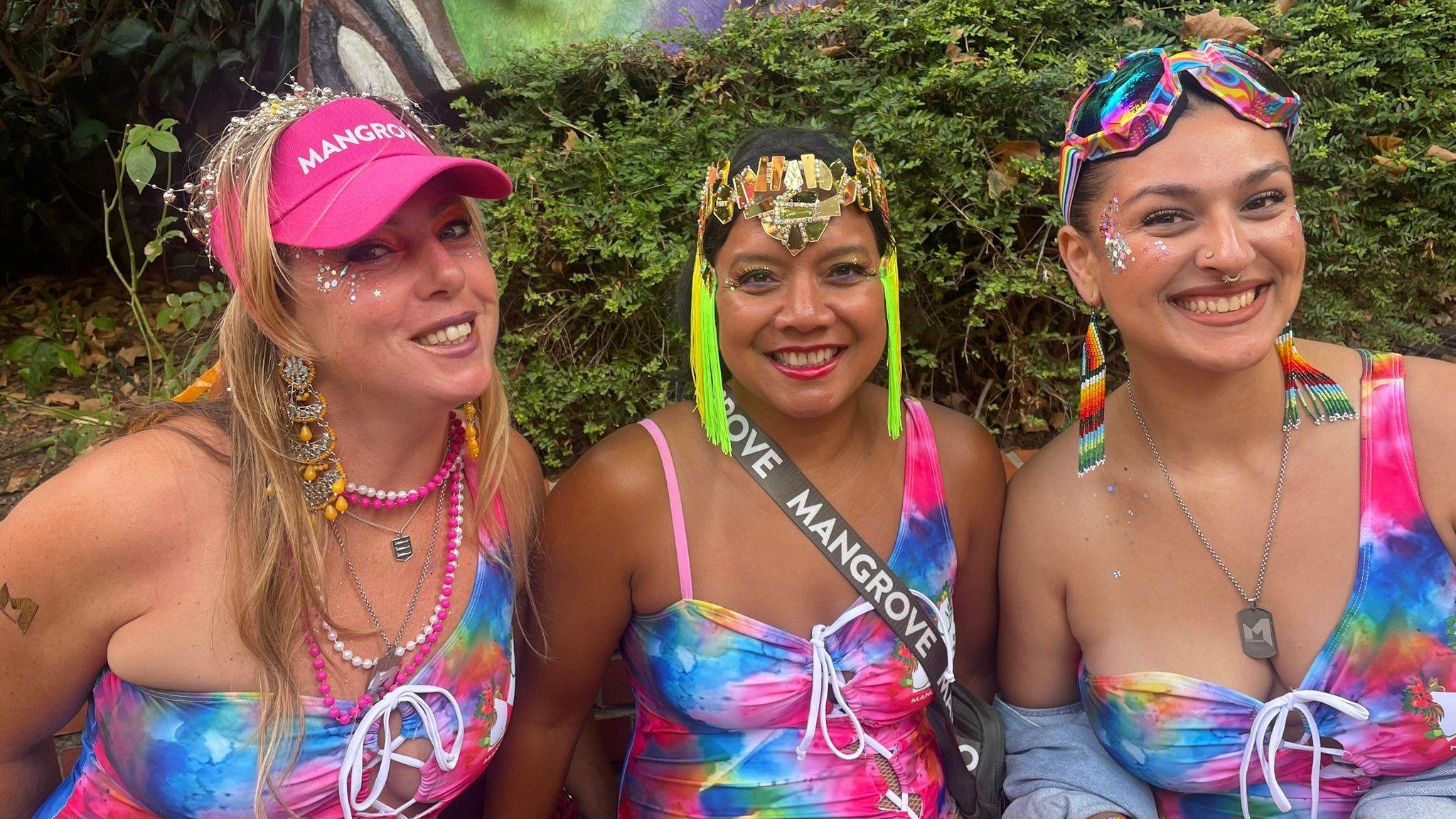Three women in brightly-coloured costumes smile.