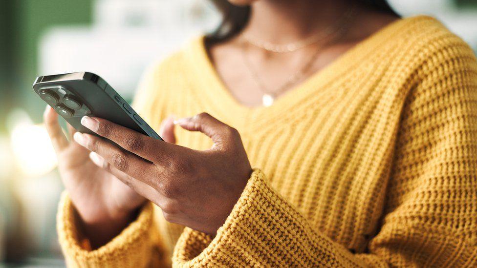 Close-up of a woman wearing a bright yellow jumper holding a smartphone.